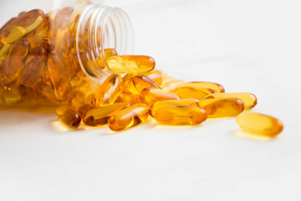 A close-up shot of a bottle of omega-3 supplement capsules, with a few capsules spilled out onto a surface.