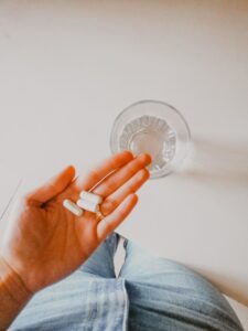 A woman holding weight loss supplements in her palm over a clear glass of water.