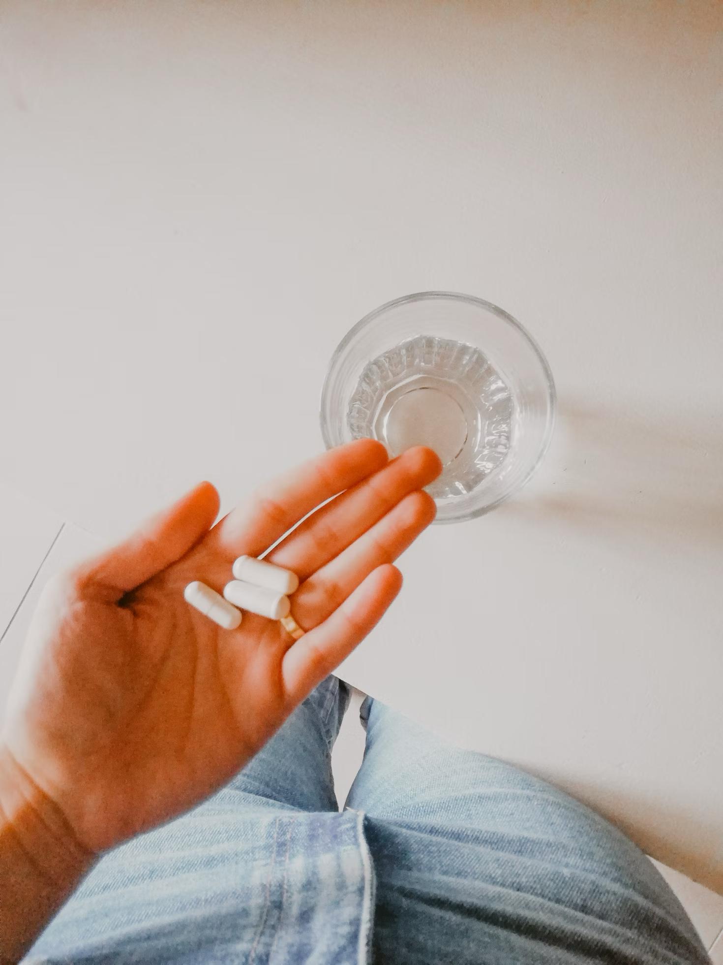 A woman holding weight loss supplements in her palm over a clear glass of water.