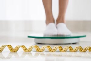 Woman standing on a weighing scale with a measuring tape on the floor.