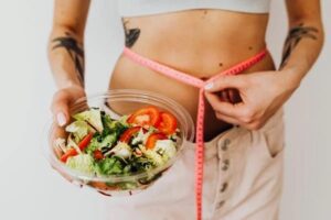 Woman measuring her waistline while holding a bowl of salad for weight loss and fixing slow metabolism.