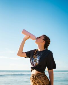 Woman drinking water by the sea to support hydration and fat loss