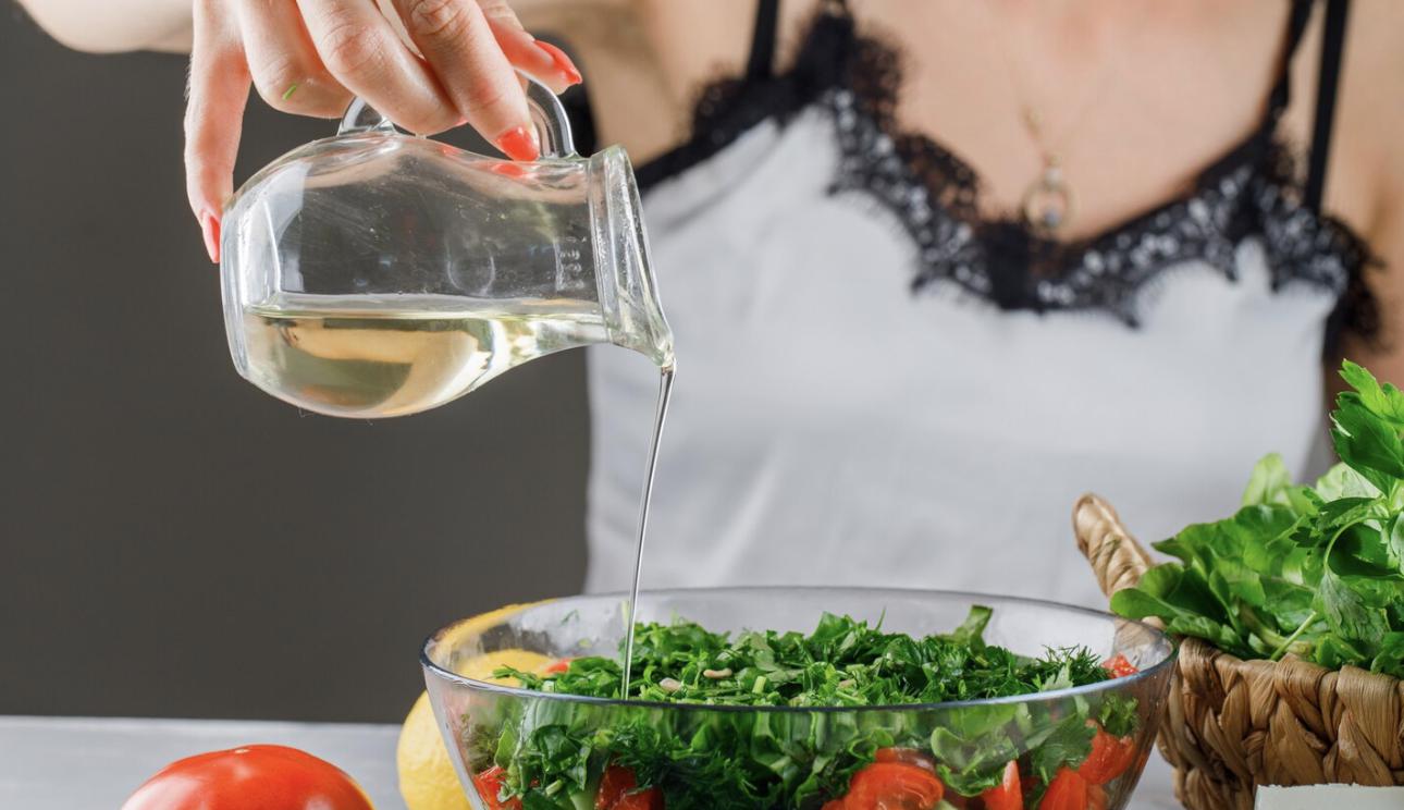 A woman liberally pouring dressing onto a salad.